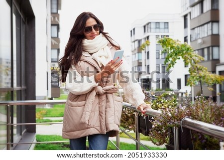 Fashionable woman dressed beige quilted oversize gilet with belt, warm white knitted sweater, scarf, jean. Trend women's clothing for autumn or spring