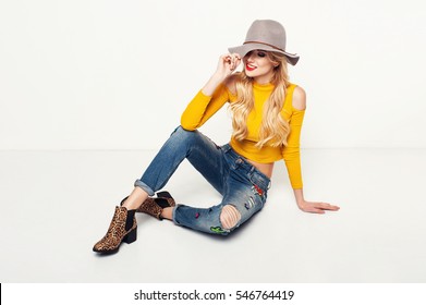 Fashionable Woman In A Hat, Boots And Jeans, Posing In A Studio. Fashion Photo