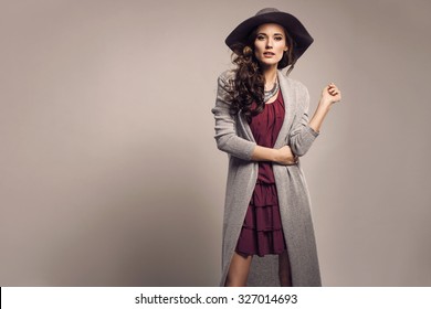 Fashionable Woman In A Hat, Dress And Long Grey Sweater, Accessories, High Heels, Posing In Studio. Fashion Autumn Photo