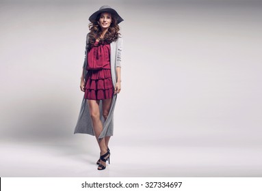 Fashionable Woman In A Hat, Dress And Long Grey Sweater, Posing In Studio. Fashion Autumn Photo. Wonderful Hair Style