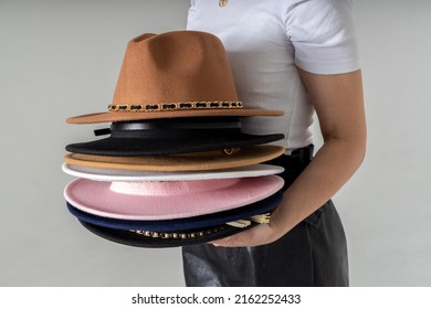 Fashionable woman with many hats, posing on gray background. Fashion, sale, shopping advertising conception. Copy, empty space for text. Sets of hats close up. Variety of hats in hands.