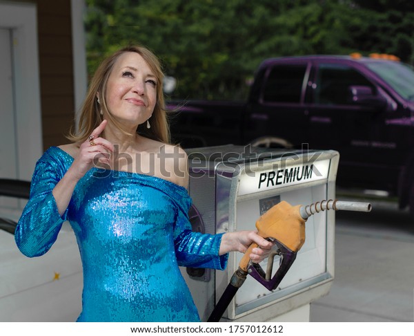 Fashionable woman in sparkling evening\
dress considers pumping premium gas at service\
station
