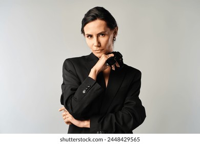 A fashionable woman in sunglasses confidently poses in a sleek black suit against a grey studio backdrop. - Powered by Shutterstock