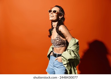 A fashionable woman wearing a leopard print top and denim shorts, exuding confidence and style on an orange background. - Powered by Shutterstock