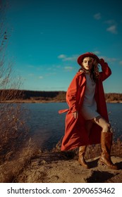 Fashionable Woman Wearing Stylish White Mini Dress, Long Orange Trench Coat, Hat, Brown Leather High Boots, Posing In Nature. Outdoor Full-length Autumn Fashion Portrait