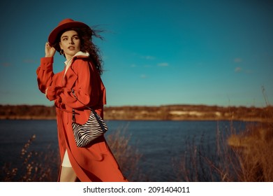 Fashionable Woman Wearing Trendy Orange Trench Coat, Hat, Holding Zebra Print Faux Leather Handbag, Posing In Nature. Outdoor Autumn Fashion Portrait. Copy, Empty Space For Text