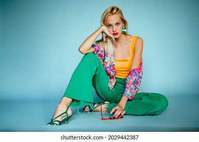 Fashionable woman wearing trendy summer outfit: orange top, colorful shirt, green wide leg jeans, strappy sandals. Full-length studio fashion portrait. Copy, empty space for text
