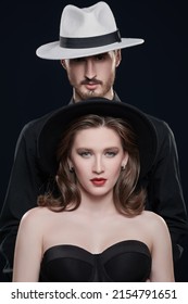 Fashionable Young Couple In Elegant Black Evening Clothing And Hats. Studio Portrait On A Black Background. Love And Fashion. 