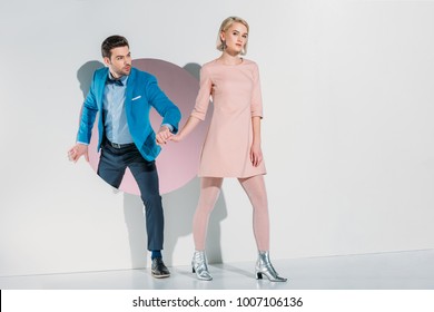 Fashionable Young Couple Holding Hands And Walking Through Hole On Grey