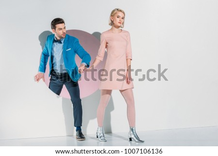 fashionable young couple holding hands and walking through hole on grey