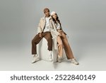 A fashionable young couple relaxes on a pedestal, radiating autumn vibes with trendy outfits.