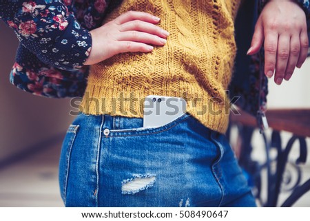 Fashionable young girl carrying new smartphone with dual camera in jeans pocket.Young woman with big mobile phone.Trendy female with new silver cellphone in pocket