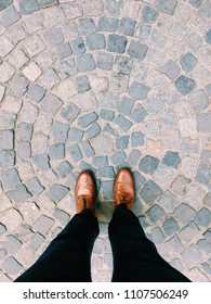 Fashionable Young Man With Brown Leather Shoes Standing On Cobblestone Paved Street. Perspective View Looking Down