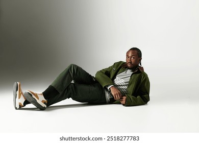 A fashionable young man lounges gracefully on the floor, showcasing his trendy green outfit with flair. - Powered by Shutterstock