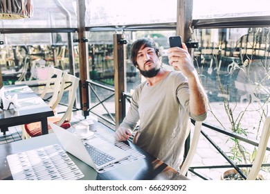 Fashionable Young Man Taking Pictures Of Himself At Work. Young Hipster Making Selfie In Cafe