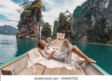fashionable young model in boho style dress lying on boat at the lake 