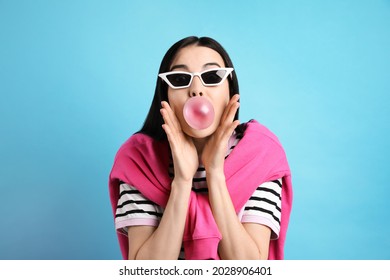 Fashionable Young Woman Blowing Bubblegum On Light Blue Background