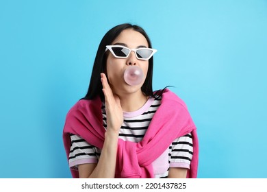 Fashionable Young Woman Blowing Bubblegum On Light Blue Background