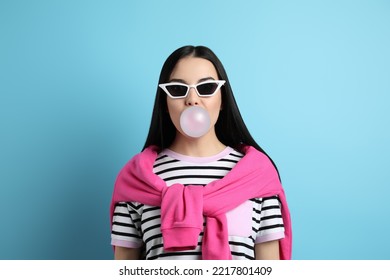 Fashionable Young Woman Blowing Bubblegum On Light Blue Background