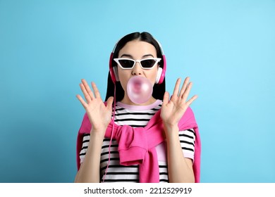 Fashionable Young Woman With Headphones Blowing Bubblegum On Light Blue Background