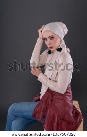 Fashionable young woman in jeans, long sleeves leather jacket and hijab isolated on grey background. Stylish Muslim female hijab fashion lifestyle portraiture concept.