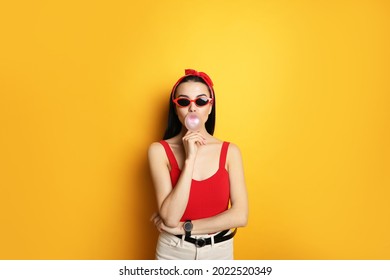 Fashionable Young Woman In Pin Up Outfit Blowing Bubblegum On Yellow Background