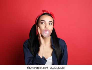 Fashionable Young Woman In Pin Up Outfit Blowing Bubblegum On Red Background