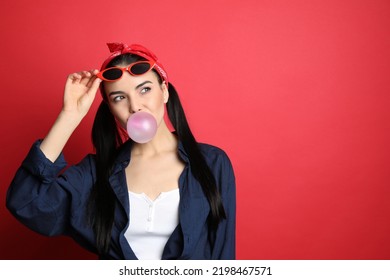 Fashionable Young Woman In Pin Up Outfit Blowing Bubblegum On Red Background, Space For Text