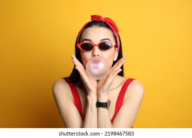 Fashionable Young Woman In Pin Up Outfit Blowing Bubblegum On Yellow Background