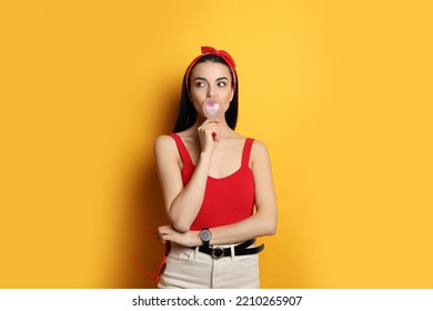 Fashionable Young Woman In Pin Up Outfit Blowing Bubblegum On Yellow Background