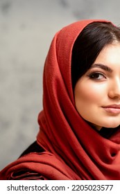 The Fashionable Young Woman. Portrait Of The Beautiful Female Model With Long Hair And Makeup In A Red Scarf. Beauty Young Caucasian Woman On The Background Of A Gray Wall