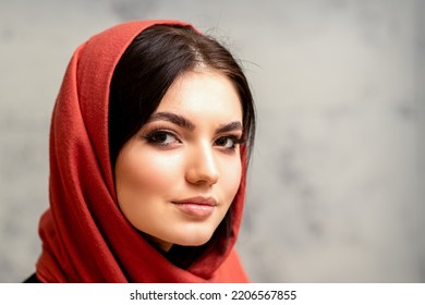 The Fashionable Young Woman. Portrait Of The Beautiful Female Model With Long Hair And Makeup In A Red Scarf. Beauty Young Caucasian Woman On The Background Of A Gray Wall