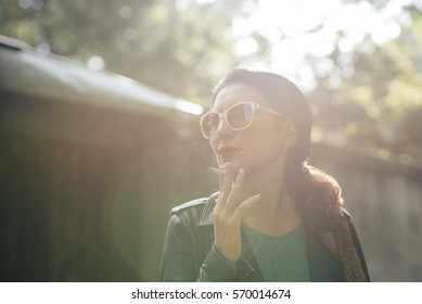 Fashionable Young Woman Smoking Cigarette Outside On Sunny Day.