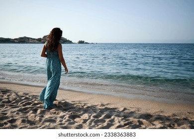 Fashionable young woman standing on tranquil beach, hair flowing, enjoying vacation in nature. - Powered by Shutterstock