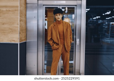 Fashionable young woman in a stylish brown suit standing in front of an elevator in a modern building - Powered by Shutterstock