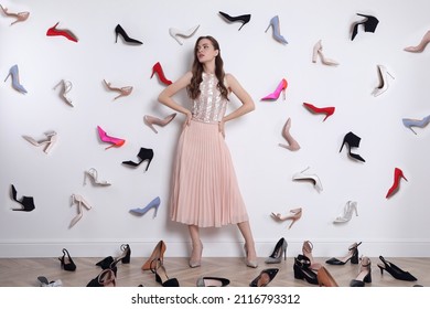 Fashionable young woman surrounded by many different high heel shoes indoors