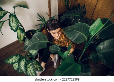Fashionable young woman taking care of her house plants and sitting next to them. Greenery at home. Love of plants. Indoor cozy garden. Copy space. - Shutterstock ID 2227722399
