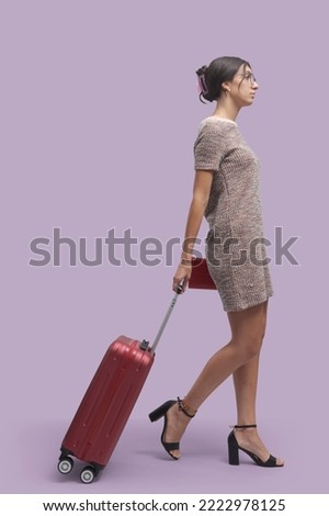 Fashionable young woman traveling alone, she is walking and pulling a trolley bag