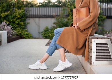 Fashionable Young Woman Wearing Beige Wool Coat And Blue Jeans. She Is Holding Trendy Tan Tote Bag In Hands. Street Style. 