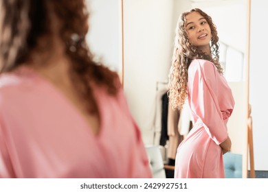 Fashionable youngster girl exuding confidence and wellness as she admires herself in the mirror, wearing elegant pink dress, preparing from school prom. Joy of self expression through style - Powered by Shutterstock