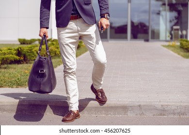 fashionably dressed businessman walks from office building with a bag and car keys in his hand.