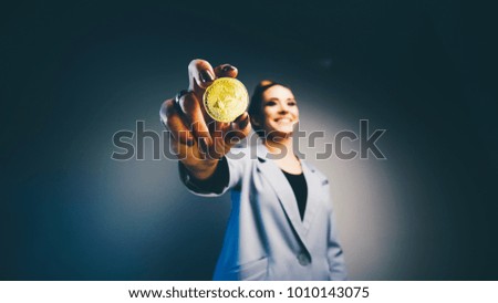 fashioned woman in business suit holding golden coin bitcoin in hand, blured woman figure from below view