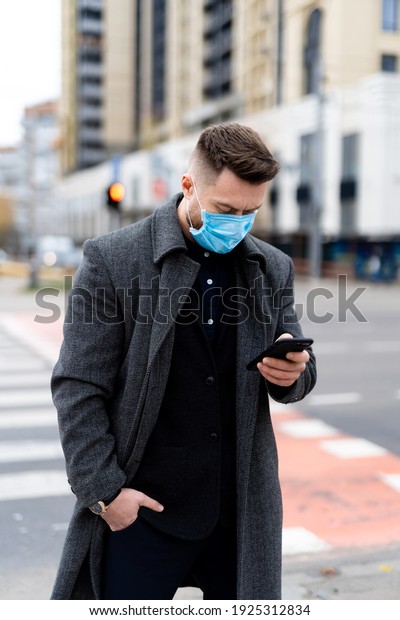 Fasionable man in formal clothes wearing safety\
mask and using phone outside. Responsible behavior during world\
covid-19 pandemic.
