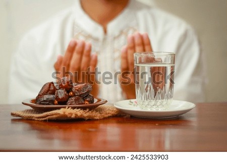 Fast breaking meal or iftar dish with muslim man hands praying to Allah. Dates with a glass of mineral water on the table.Traditional Ramadan, fast breaking meal.Buka puasa or sahur Ramadan concept.