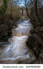 A Fast Flowing River In A Gulley With A Viaduct Behind. Merthyr Tydfil, UK