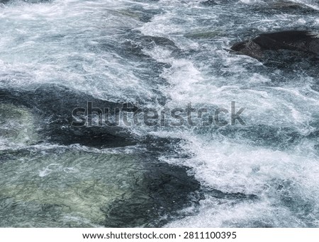 Fast Flowing River Rapids Over Dark Natural Rocks - Powerful river current with splashing water and textured rocks, perfect for nature and adventure concepts.