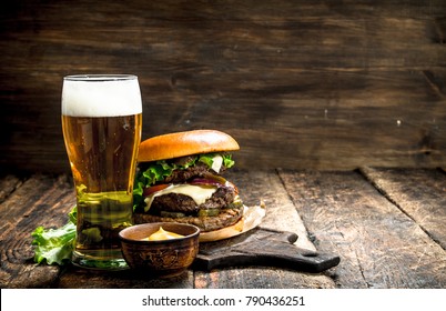 Fast food. A big burger with beef and a glass of beer. On a wooden background.