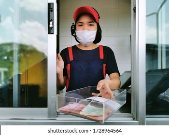 Fast Food Cashier In Drive Thru Service Waring Hygiene Face Mask To Protect Coronavirus Pandemic Or Covid-19 Virus Outbreak Is Giving Money Change To Customer.