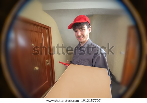 Fast food delivery man with pizza box in his\
hands delivering the order, dressed in uniform and smiling,\
customer looking through the\
peephole