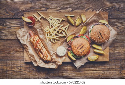 Fast Food Dish Top View. Appetizing Meat Burgers, Potato Chips And Wedges With Hot Dog. Takeaway Composition. French Fries, Hamburger And Sauces On Wood With Copy Space. Menu Or Receipt Mockup